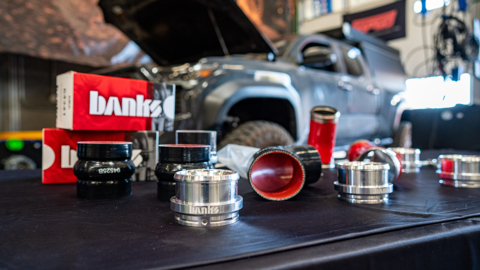 Banks 26012 kit laid out at SDHQ Off-Road: billet aluminum quick-connect adapters engraved Banks, black and red silicone couplers, and Banks retail boxes, with the 4G Tacoma on the lift behind
