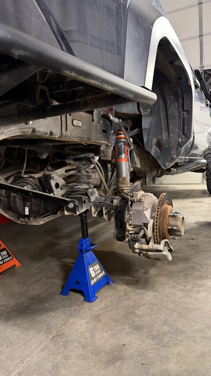 Tacoma rear suspension with the wheel removed, showing the FOX shock, coil spring, links, and 74Weld portal hub before the new bump-stop mount