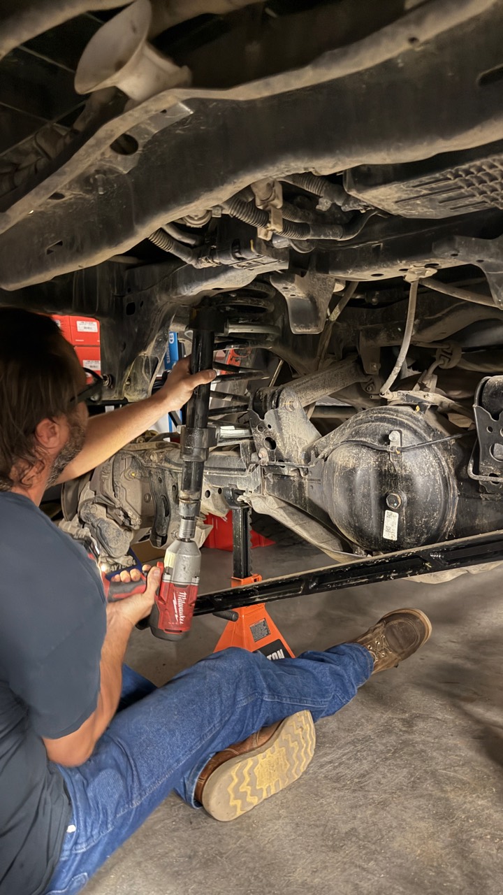 Rear suspension work underway beneath the Tacoma, with the axle supported and coil spring exposed