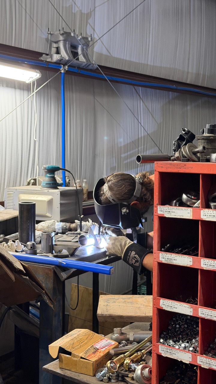 Fabrication work at Arizona Chassis Engineering, with a welder joining tubular mounting components on the bench