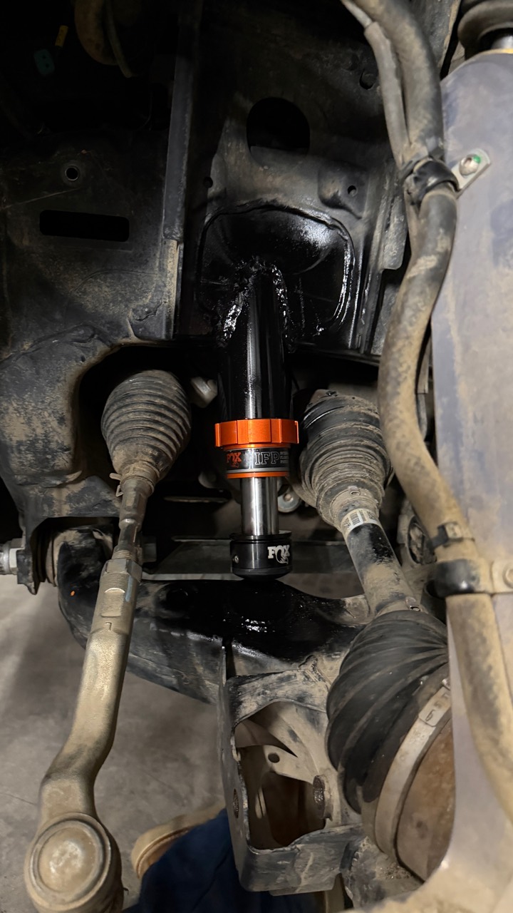 Installed front FOX IFP hydraulic bump stop in a coated custom mount above a lower-control-arm strike surface