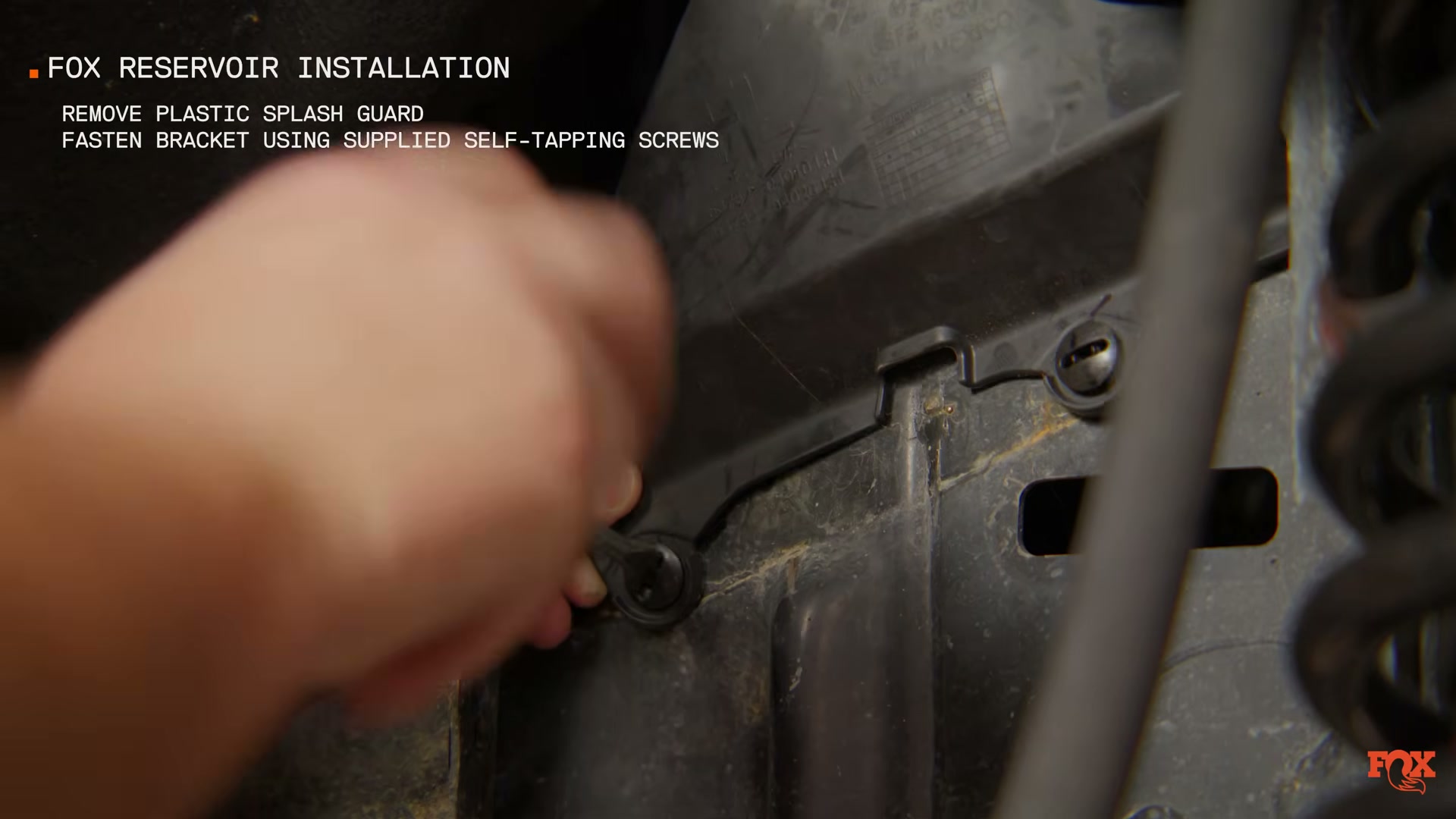 Fox reservoir bracket installation on Tacoma frame rail using self-tapping screws — source: Fox Racing