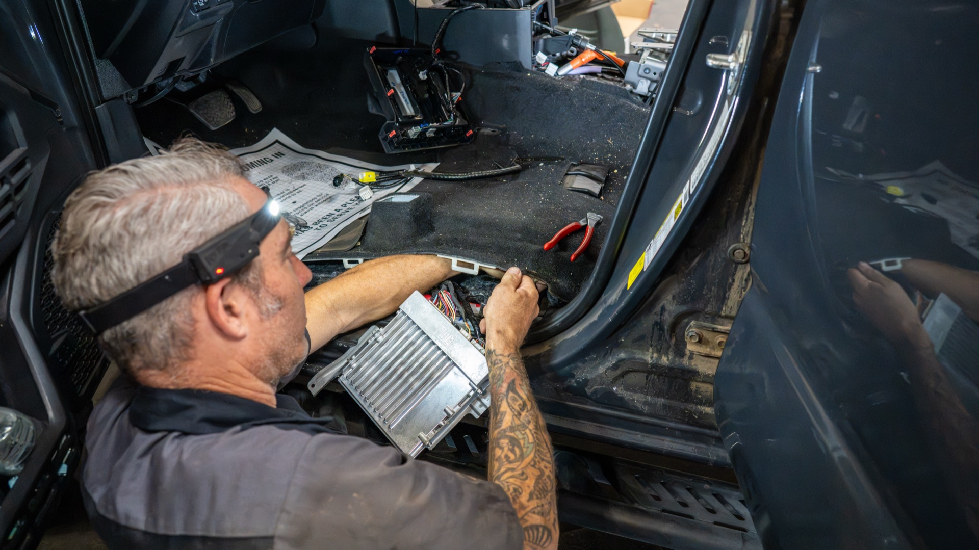 SDHQ tech fitting the finned Fox ECU at the driver's door sill of my Tacoma, carpet peeled back and install manual on the floor — photo: SDHQ Off Road