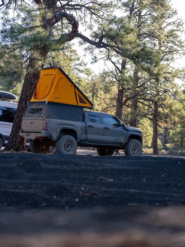 Tacoma with GFC camper tent up in a forest clearing at dusk